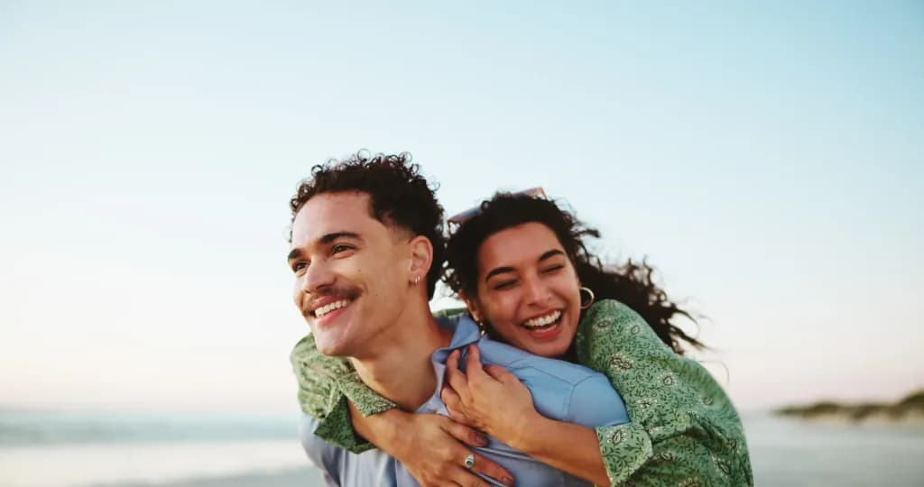 Piggy back, laugh and couple at beach for romantic vacation, holiday and weekend outdoors. Travel, nature and man carry woman by sea, ocean and bonding on adventure, journey and happy together